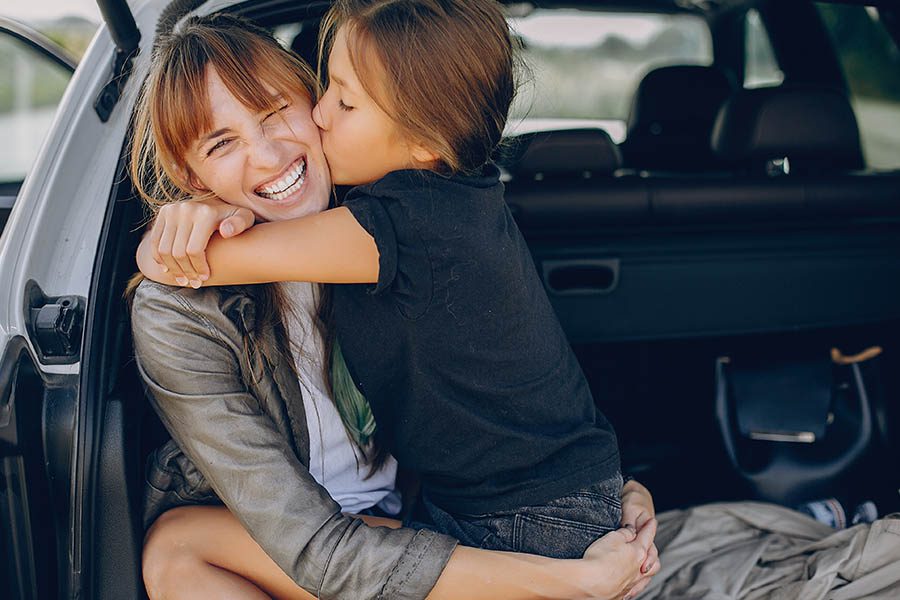Personal Insurance - Mother and Daughter Sitting in the Trunk of Car Before a Road Trip